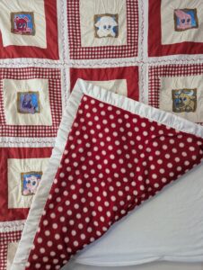 The plush red and white polka dot minky backing of a handmade Barnyard Besties baby quilt, folded back to showcase the smooth white satin ruffle border.