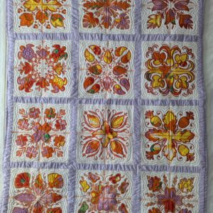 A Hawaiian-style wall quilt with a 3x4 grid of white squares. Each square features a unique tropical appliqué design—including turtles, pineapples, and flowers—made from orange, yellow, and purple patterned fabric. The squares are separated by light purple sashing with a matching purple border.