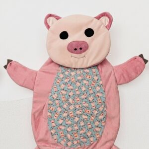 Plush handcrafted pig-shaped tummy time mat for babies, featuring a blue cotton center with a piglet print and a soft magenta plush body.