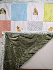 The plush, sage green minky faux fur backing of a handmade Lion King baby quilt, folded back to reveal the silky mint green satin trim.