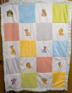 Handmade patchwork baby quilt featuring embroidered Lion King characters, textured minky squares, and a mint green satin ruffle border.